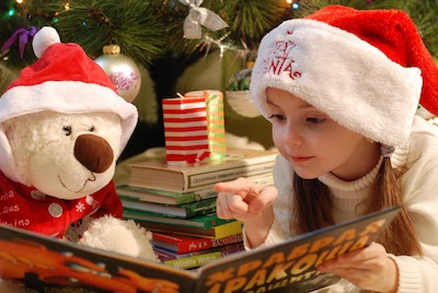 Child reading book to teddybear at christmas