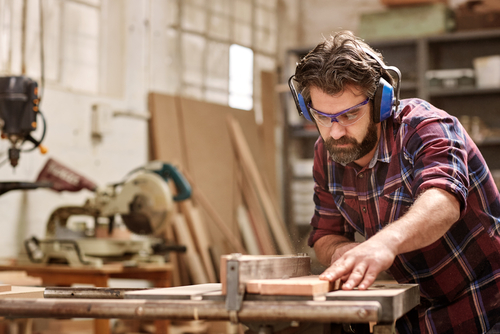 man in woodshop using saw while wearing protective eyewear 