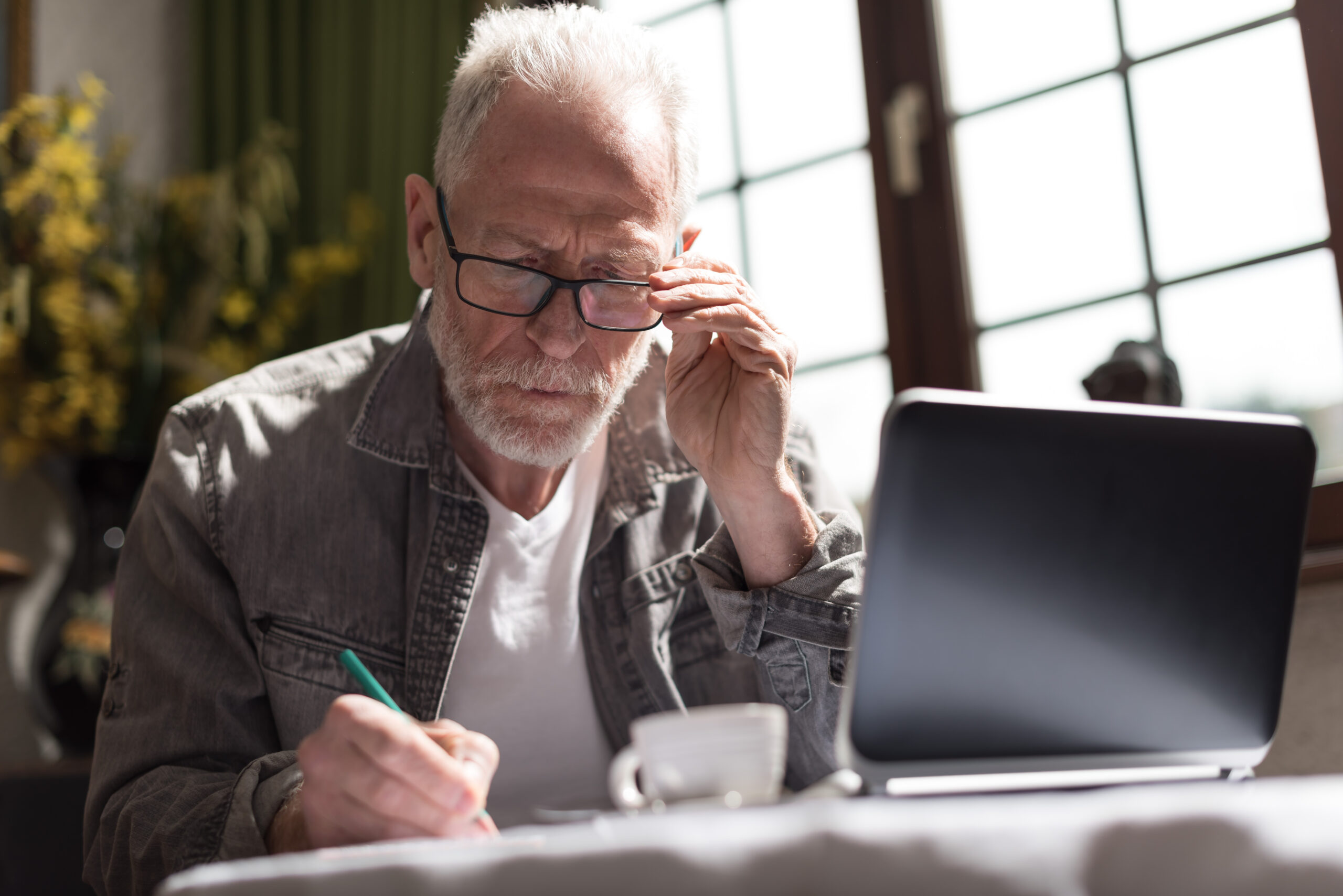 man sitting at table with laptop and coffee while writing notes